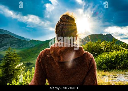 Beschreibung: Sportliche Frau in Outdoor-Jacke sieht sich die wunderschöne Bergkulisse bei Sonnenuntergang an. Falzarego Pass, Dolomiten, Südtirol, Italien, Europa. Stockfoto