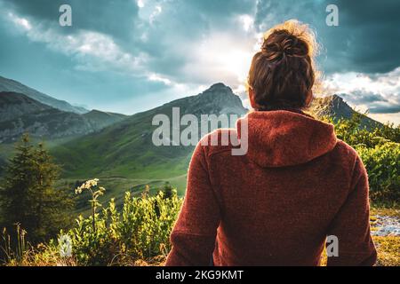 Beschreibung: Sportliche Frau in Outdoor-Jacke sieht sich die wunderschöne Bergkulisse bei Sonnenuntergang an. Falzarego Pass, Dolomiten, Südtirol, Italien, Europa. Stockfoto