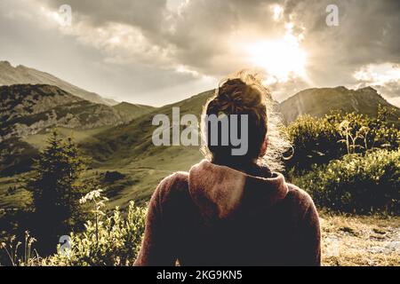 Beschreibung: Sportliche Frau in Outdoor-Jacke sieht sich die wunderschöne Bergkulisse bei Sonnenuntergang an. Falzarego Pass, Dolomiten, Südtirol, Italien, Europa. Stockfoto