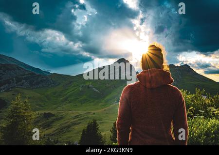 Beschreibung: Sportliche Frau in Outdoor-Jacke sieht sich die wunderschöne Bergkulisse bei Sonnenuntergang an. Falzarego Pass, Dolomiten, Südtirol, Italien, Europa. Stockfoto