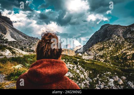 Beschreibung: Sportliche Frau in Outdoor-Jacke sieht sich die wunderschöne Bergkulisse bei Sonnenuntergang an. Falzarego Pass, Dolomiten, Südtirol, Italien, Europa. Stockfoto