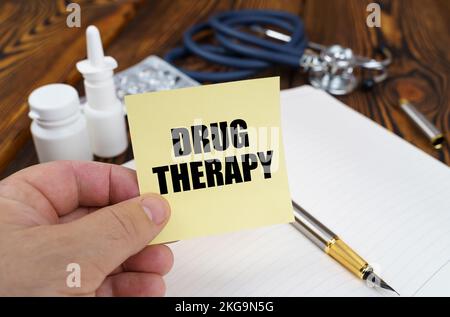 Medizinisches Konzept. Auf dem Tisch liegen ein Notizbuch, Medikamente und ein Stethoskop in den Händen eines Aufklebers mit der Aufschrift "Drug Therapy" Stockfoto