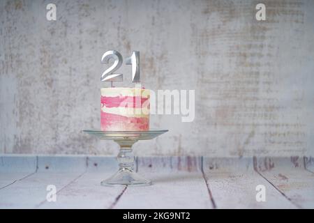 21. Geburtstagskuchen, rosa und silberne Torte mit ein paar Streuseln und 21. Kerzenlicht auf weißem Holzhintergrund. Stockfoto