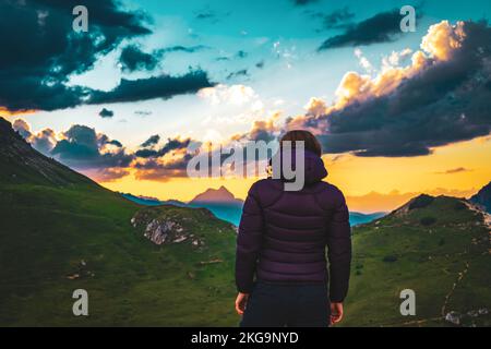 Beschreibung: Sportliche Frau in Outdoor-Jacke sieht sich wunderschöne Sonnenuntergänge in den Bergen an. Falzarego Pass, Dolomiten, Südtirol, Italien, Europa. Stockfoto