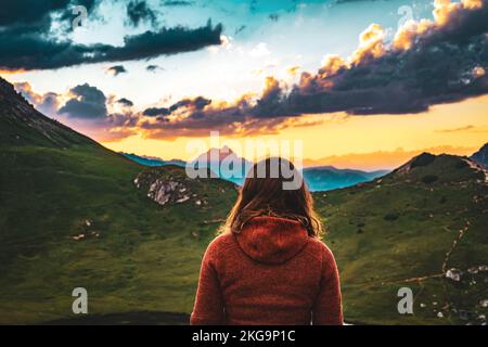 Beschreibung: Sportliche Frau in Outdoor-Jacke sieht sich wunderschöne Sonnenuntergänge in den Bergen an. Falzarego Pass, Dolomiten, Südtirol, Italien, Europa. Stockfoto