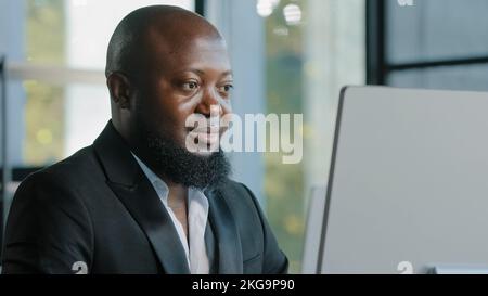 Afrikanischer Erwachsener Geschäftsmann glücklich plus Größe Kerl zufrieden mit Computer-App-Eingabe auf Laptop im Büro lächelnd empfehlen gute Wahl feine Idee Zeichen Stockfoto
