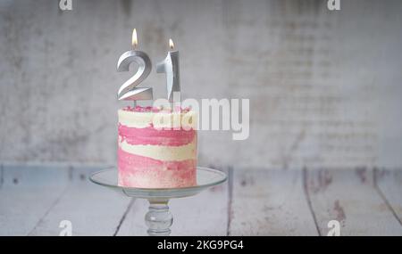 21. Geburtstagskuchen, rosa und silberne Torte mit ein paar Streuseln und 21. Kerzenlicht auf weißem Holzhintergrund. Stockfoto