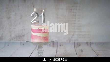 21. Geburtstagskuchen, rosa und silberne Torte mit ein paar Streuseln und 21. Kerzenlicht auf weißem Holzhintergrund. Stockfoto