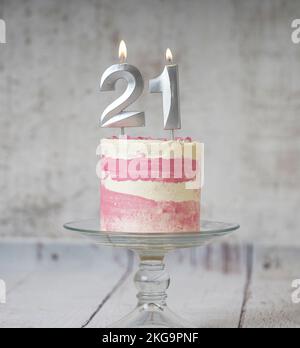 21. Geburtstagskuchen, rosa und silberne Torte mit ein paar Streuseln und 21. Kerzenlicht auf weißem Holzhintergrund. Stockfoto