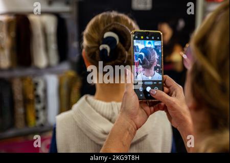 Eine Barbierin, die mit einem Smartphone ein Foto von der Frisur ihres Kunden macht Stockfoto