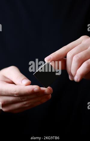 Die Hände eines Mannes halten eine quadratische kleine schwarze Box mit einem leeren Platz für Text und Design isoliert auf dunklem Hintergrund. Board, leer, Vorlage, Modell, Layout für einen Slogan oder eine Inschrift Stockfoto