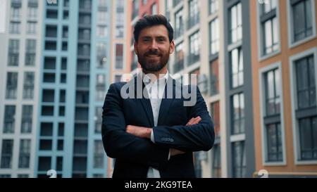 Selbstbewusster Chef, erfolgreicher Geschäftsmann, männlicher Architekt, der in selbstbewusster Pose steht, mit gekreuzten Armen allein auf der Straße der Stadt, Outdoor Modern Stockfoto