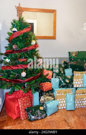 Großer, schöner Weihnachtsbaum, dekoriert mit wunderschönen glänzenden Ornamenten und vielen verschiedenen Geschenken auf dem Boden. Weißer Hintergrund mit vielen Kopien Stockfoto