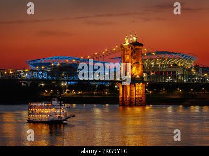 John A Roebling Hängebrücke in der Dämmerung. Paul Brown Stadium, Paycor Stadium, Heimstadion der Fußballmannschaft Cincinnati Bengals, im Hintergrund. Belle Stockfoto