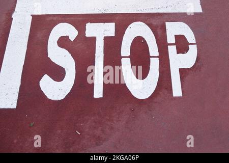 Detail eines Verkehrsschilds, das auf dem Asphalt mit dem Wort STOP aufgedruckt ist, sodass Fahrzeuge an dieser Stelle anhalten Stockfoto