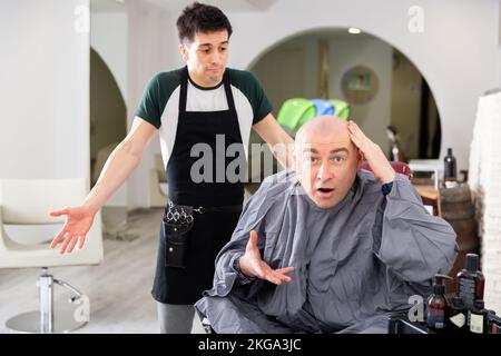 Unzufriedener Mann mit rasierten Kopf im Friseurladen Stockfoto