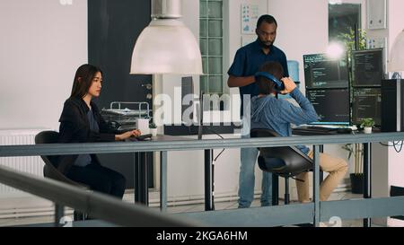 Unterschiedliches Team von Software-Ingenieuren, die Servercode in das Terminalfenster schreiben und dabei ein Skript für die App-Entwicklung verwenden. Datenbankadministratoren entwickeln Algorithmen mit Programmiersprache. Stativaufnahme. Stockfoto