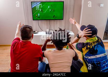 Rückansicht von Freunden, die sich ein Fußballspiel im Fernsehen ansehen und ihr Team unterstützen. Spaß beim Anfeuern der Fußballmannschaften. Stockfoto