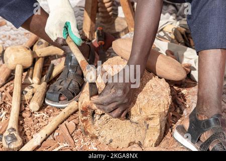 Freiluftszene in Nahaufnahme und horizontaler Ansicht der Hände eines jungen Bildhauers Afrikas, der eine Holzfigur geschnitzt hat Stockfoto