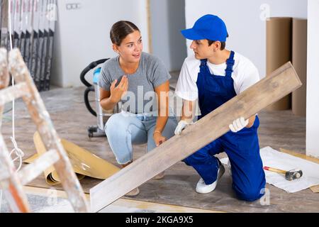 Eine Innenarchitektin, die mit dem Baumeister spricht und Laminatböden drinnen legt Stockfoto