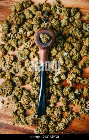Holzpfeife zum Rauchen von Marihuana auf dem Tisch vor dem Hintergrund einer Knospe von cbd sativa oder indica tgk. Arzneimittel und Medizin Stockfoto