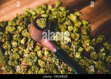 Holzpfeife zum Rauchen von Marihuana auf dem Tisch vor dem Hintergrund einer Knospe von cbd sativa oder indica tgk. Arzneimittel und Medizin Stockfoto