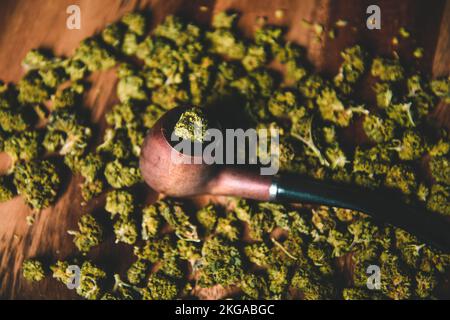 Holzpfeife zum Rauchen von Marihuana auf dem Tisch vor dem Hintergrund einer Knospe von cbd sativa oder indica tgk. Arzneimittel und Medizin Stockfoto