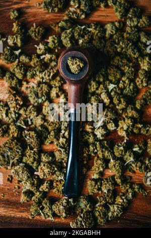 Holzpfeife zum Rauchen von Marihuana auf dem Tisch vor dem Hintergrund einer Knospe von cbd sativa oder indica tgk. Arzneimittel und Medizin Stockfoto