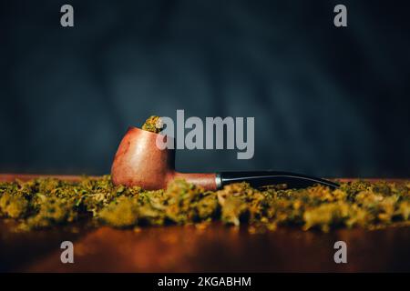 Holzpfeife zum Rauchen von Marihuana auf dem Tisch vor dem Hintergrund einer Knospe von cbd sativa oder indica tgk. Arzneimittel und Medizin auf schwarzem Hintergrund Stockfoto