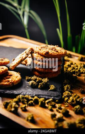 Marihuana-Kekse, Drogen in Lebensmitteln, thc und cbd-Brownies. Drogen und Marihuana-Knospen auf einer Planke vor dem Hintergrund des Wachstums Stockfoto