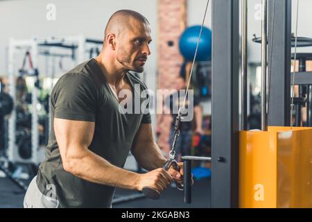 Kräftiger, muskulöser, gutaussehender Glatzkopf, Bodybuilder, der im Fitnessstudio Trizep-Verlängerungen vorführt. Hochwertiges Foto Stockfoto