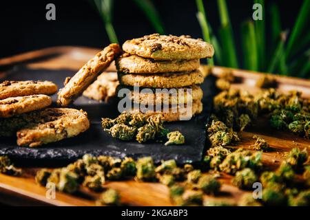 Marihuana-Kekse, Drogen in Lebensmitteln, thc und cbd-Brownies. Drogen und Marihuana-Knospen auf einer Planke vor dem Hintergrund des Wachstums Stockfoto