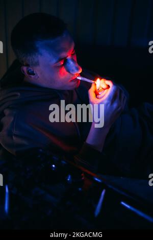 Porträt eines Mannes in Neon, der einen Joint raucht. Guy raucht Joint, Marihuana, Drogen cbd und thc Stockfoto