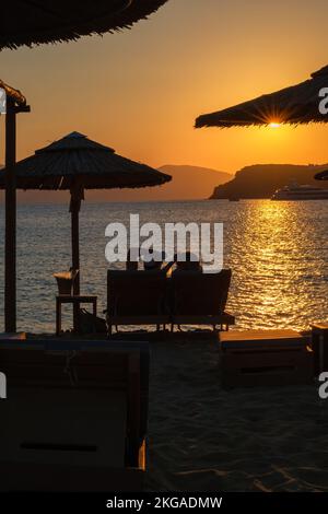 IOS, Griechenland - 13. September 2022 : Blick auf ein Paar, das auf Sonnenliegen liegt, Wein trinkt und den herrlichen Sonnenuntergang in Orange in iOS Greece genießt Stockfoto