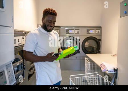 Zufriedener junger Mann, der an einem Waschsalon steht Stockfoto
