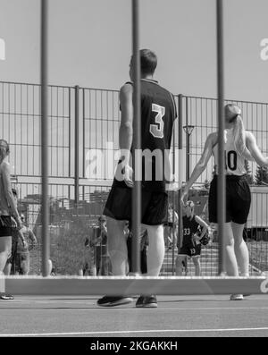 Ein Team von Studenten spielt im Sommer auf einem Sportplatz auf dem Campus im Freien Basketball. Stockfoto