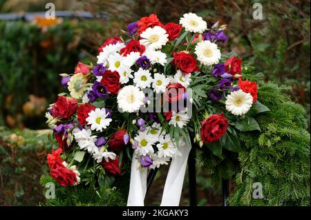 Bestattungskranz auf einem Friedhof mit bunten Blumen und Schleife auf einem Metallständer Stockfoto