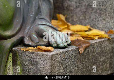 Die Hand einer Engelsfigur auf einem Stein mit Herbstblättern auf einem Friedhof Stockfoto