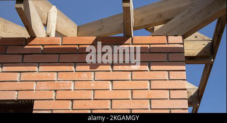 Ein privates Wohngebäude im Bau mit einer Dachkonstruktion mit Holzrahmen. Unfertiges Ziegelgebäude im Bau, Nahaufnahme. Stockfoto