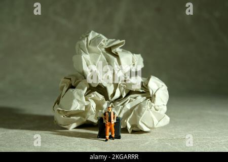 Miniatur-Menschen-Spielzeug-Figuren-Fotografie. Putzfrau mit Mülleimer, der zwischen der Papierkugel auf dem Boden läuft. Bildfoto Stockfoto