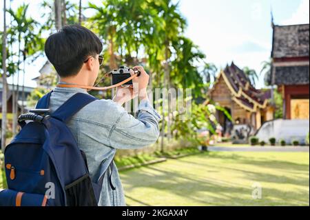 Attraktiver junger asiatischer Reisender oder Rucksacktourist, der mit seiner Retro-Kamera ein Foto des wunderschönen nordthailändischen Tempels macht. Urlaubskonzept. Stockfoto