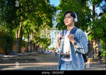 Hipster und attraktiver junger männlicher asiatischer Reisender mit seinem Rucksack und Kopfhörern schlendern gern durch die Altstadt von Chiangmai, Thailand. Asi Stockfoto