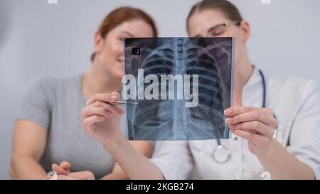 Der Arzt konsultiert eine kaukasische Frau und kommentiert die Röntgenaufnahme der Lunge. Stockfoto
