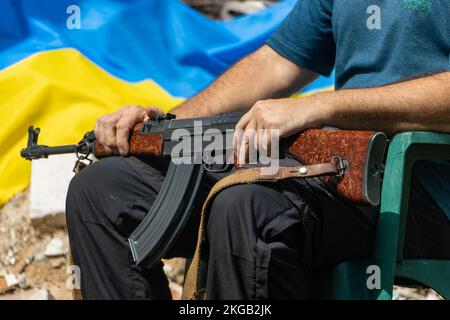 Ein Mann mit einem Sturmgewehr sitzt vor Ruinen mit ukrainischer Flagge Stockfoto