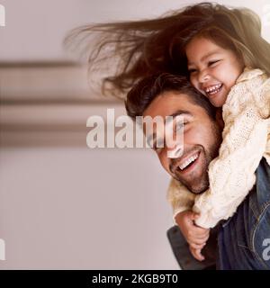 Eine Beziehung zu Dad aufbauen. Ein Vater, der seiner Tochter zu Hause einen Huckepack gibt. Stockfoto