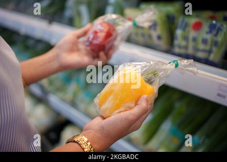 Eine Frau hält gelbe und rote Paprika im Supermarkt. Stockfoto