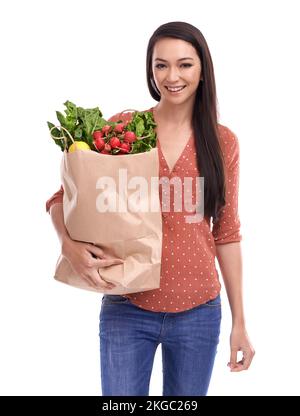 Das ist mein Lebensmitteleinkauf. Studioaufnahme einer jungen Frau, die eine Tüte mit Lebensmitteln trägt, isoliert auf Weiß. Stockfoto