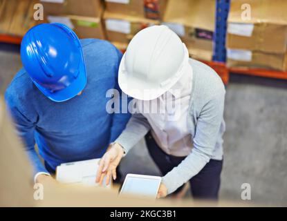 Fabrikleiter. Ein Foto von zwei Leuten mit Schutzhelm, die in einem Lagerhaus arbeiten. Stockfoto