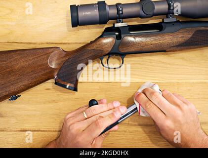 Regelmäßige Wartung ist für jeden Waffenbesitzer unerlässlich. Beschnittene Ansicht eines Mannes, der sein Gewehr putzt. Stockfoto