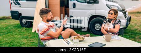 Mann, der eine Frau fotografiert, umarmt Hund mit Van und Strand im Hintergrund Stockfoto